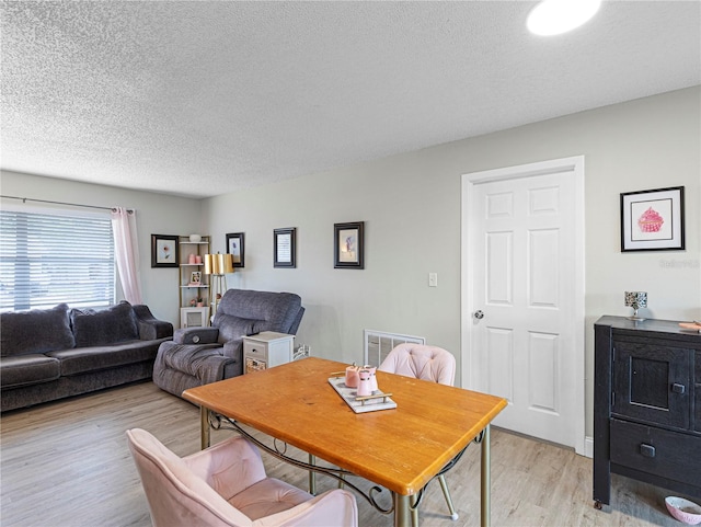 dining space with a textured ceiling, light wood finished floors, and visible vents