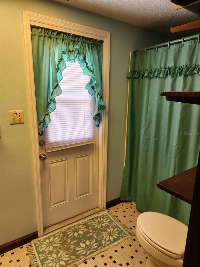 bathroom with tile patterned floors, toilet, curtained shower, and a textured ceiling