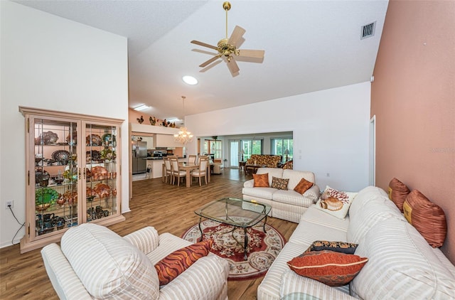 living room with ceiling fan with notable chandelier, high vaulted ceiling, and hardwood / wood-style flooring