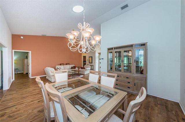 dining space with wood-type flooring, a textured ceiling, high vaulted ceiling, and an inviting chandelier