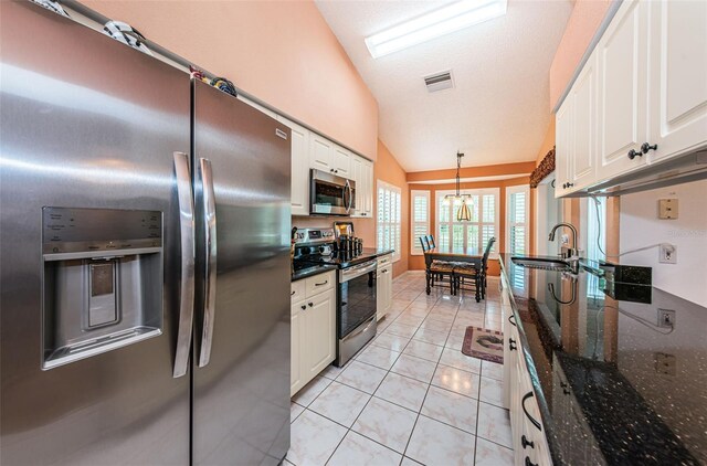 kitchen with dark stone counters, white cabinetry, light tile patterned flooring, vaulted ceiling, and appliances with stainless steel finishes