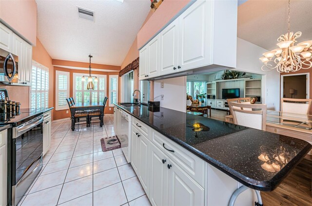 kitchen featuring appliances with stainless steel finishes, dark stone counters, vaulted ceiling, white cabinetry, and a notable chandelier