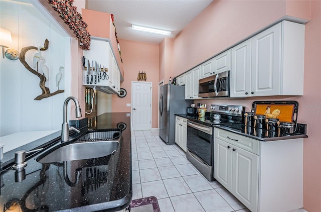 kitchen featuring appliances with stainless steel finishes, white cabinets, light tile patterned flooring, sink, and dark stone countertops