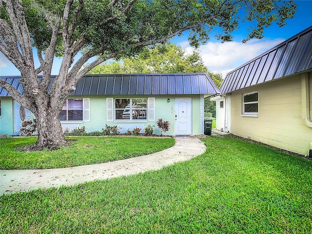 view of front facade featuring metal roof, a front yard, and stucco siding