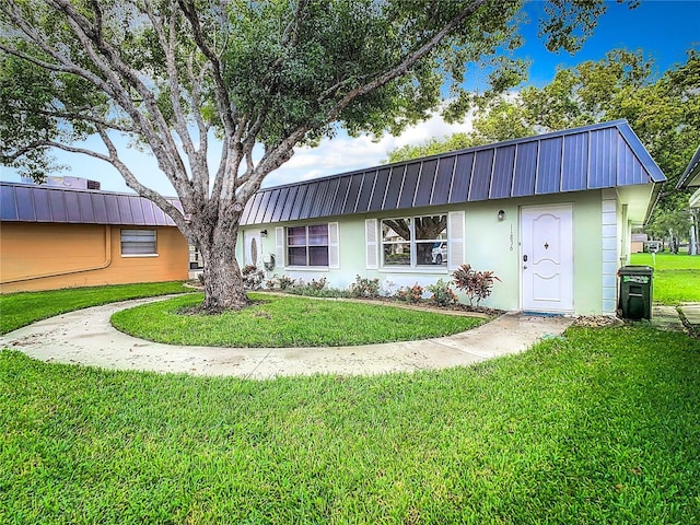 view of front of home featuring stucco siding, metal roof, and a front lawn