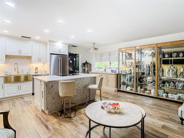 kitchen featuring high end refrigerator, a sink, light wood-style floors, light countertops, and recessed lighting