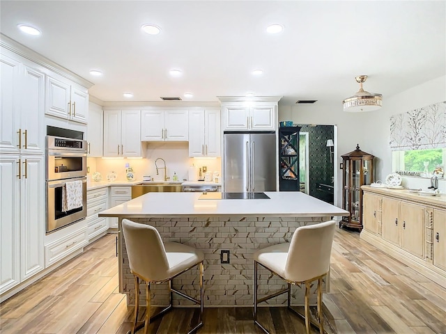 kitchen with stainless steel appliances, a sink, a kitchen bar, light wood-type flooring, and light countertops