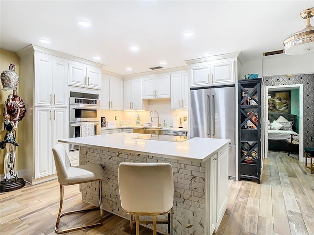 kitchen featuring stainless steel appliances, a sink, a kitchen island, light wood-type flooring, and light countertops
