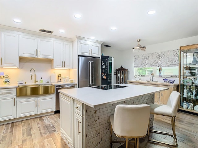 kitchen with appliances with stainless steel finishes, a sink, light wood-style flooring, a center island, and white cabinetry