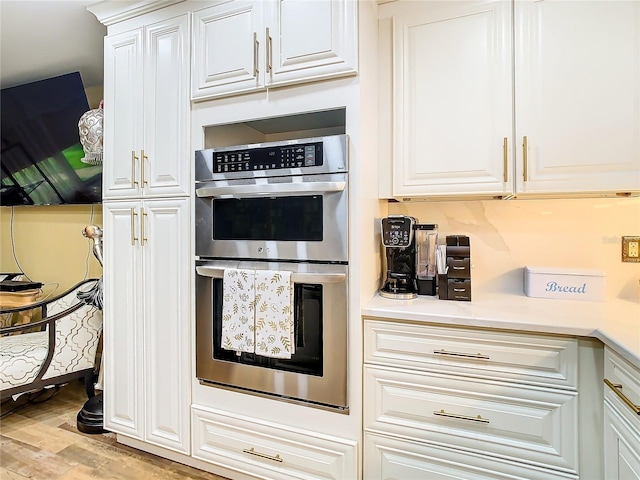 kitchen with stainless steel double oven, wood finished floors, white cabinets, and light countertops