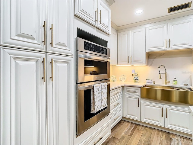 kitchen featuring double oven, a sink, white cabinets, light countertops, and recessed lighting