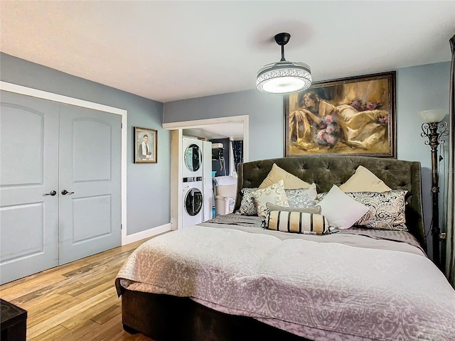 bedroom featuring stacked washing machine and dryer, wood finished floors, baseboards, and a closet