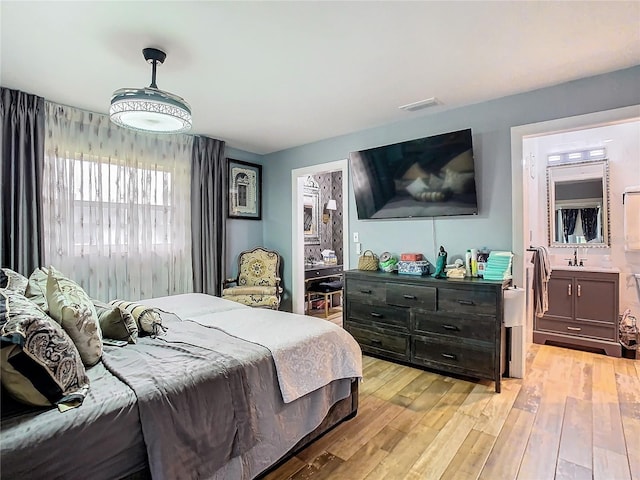 bedroom featuring light wood-style flooring, a sink, and ensuite bath