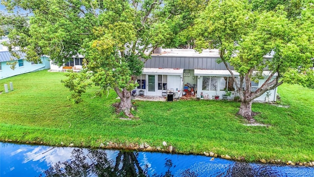 rear view of property with a yard, a water view, and metal roof