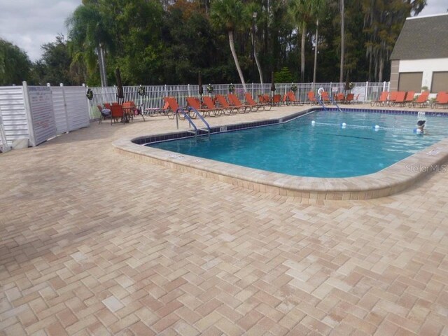 community pool with fence, a patio area, and view of scattered trees