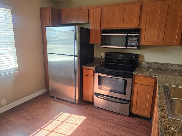 kitchen featuring sink, dark hardwood / wood-style flooring, dark stone countertops, and stainless steel appliances