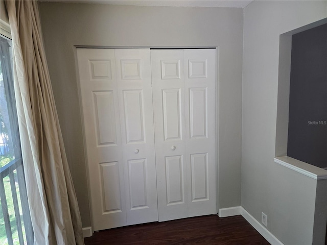 unfurnished bedroom featuring baseboards, dark wood-style floors, and a closet