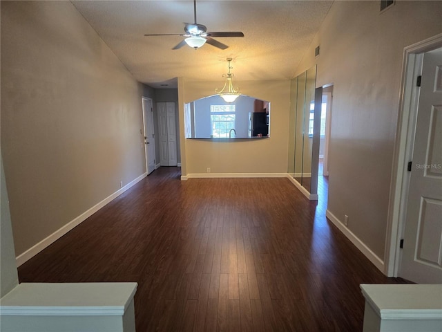 interior space with a ceiling fan, baseboards, visible vents, and dark wood-style floors