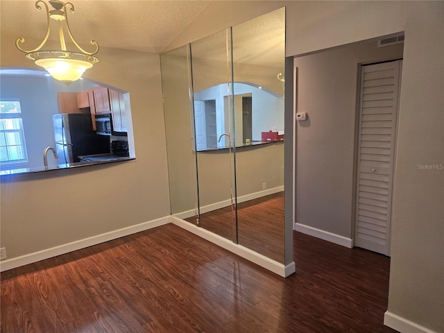 unfurnished bedroom with freestanding refrigerator, baseboards, wood finished floors, vaulted ceiling, and visible vents