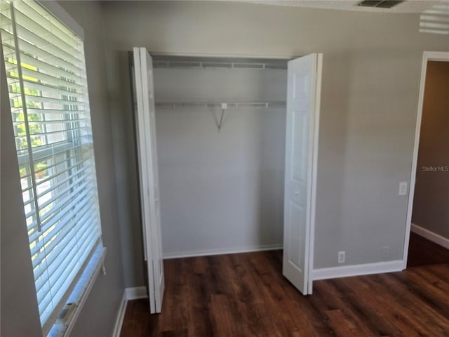 unfurnished bedroom featuring a closet, baseboards, wood finished floors, and visible vents