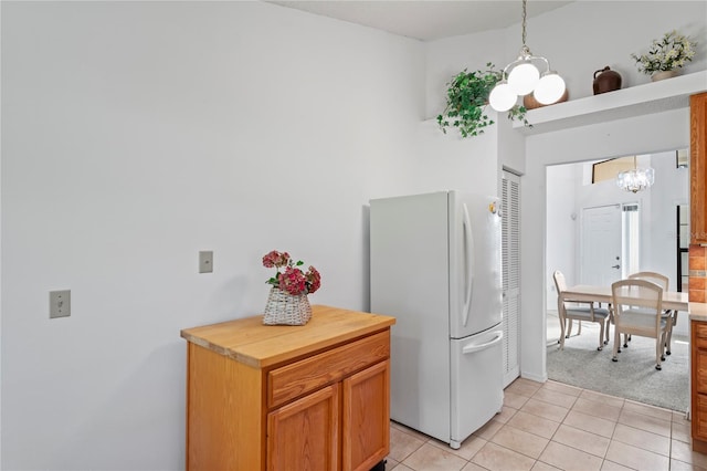 kitchen featuring pendant lighting, light tile patterned floors, white refrigerator, an inviting chandelier, and butcher block counters