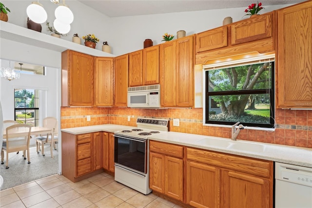 kitchen featuring decorative light fixtures, vaulted ceiling, an inviting chandelier, white appliances, and sink