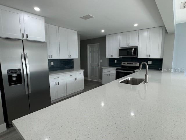 kitchen featuring backsplash, stainless steel appliances, light stone countertops, and white cabinetry