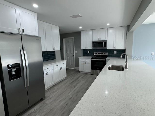 kitchen with appliances with stainless steel finishes, white cabinetry, hardwood / wood-style flooring, and sink