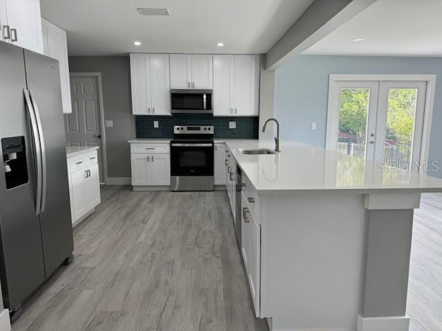 kitchen with white cabinets, appliances with stainless steel finishes, kitchen peninsula, and sink