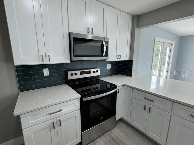 kitchen with light hardwood / wood-style flooring, appliances with stainless steel finishes, white cabinets, and decorative backsplash