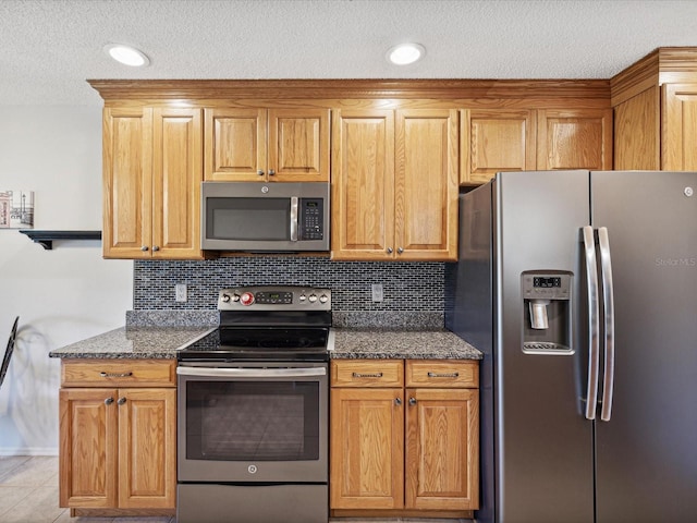 kitchen featuring light tile patterned floors, stainless steel appliances, a textured ceiling, decorative backsplash, and dark stone counters