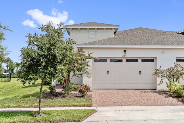 view of front of property featuring stucco siding, roof with shingles, an attached garage, decorative driveway, and a front yard