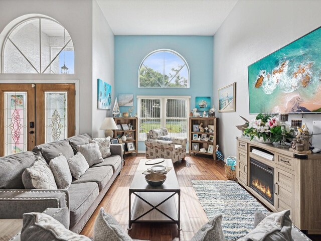 living room featuring a towering ceiling, light hardwood / wood-style flooring, and french doors