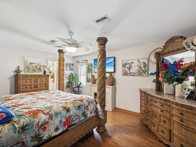 bedroom featuring ceiling fan, light hardwood / wood-style floors, a textured ceiling, and ornate columns