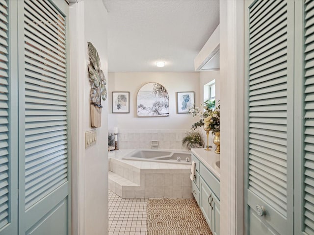 bathroom with tile patterned flooring, vanity, tiled bath, and a textured ceiling