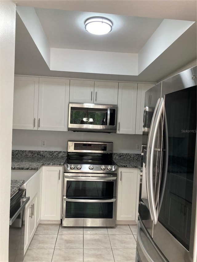 kitchen with a tray ceiling, stainless steel appliances, white cabinets, and light tile patterned floors