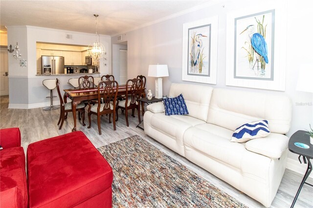 living room with an inviting chandelier, ornamental molding, and light hardwood / wood-style floors