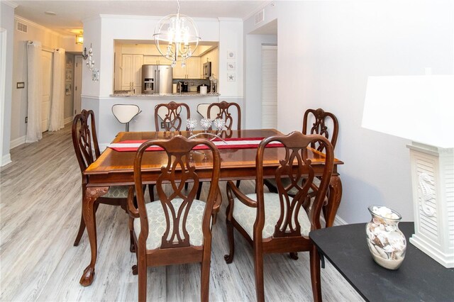 dining space featuring crown molding, an inviting chandelier, and light hardwood / wood-style floors