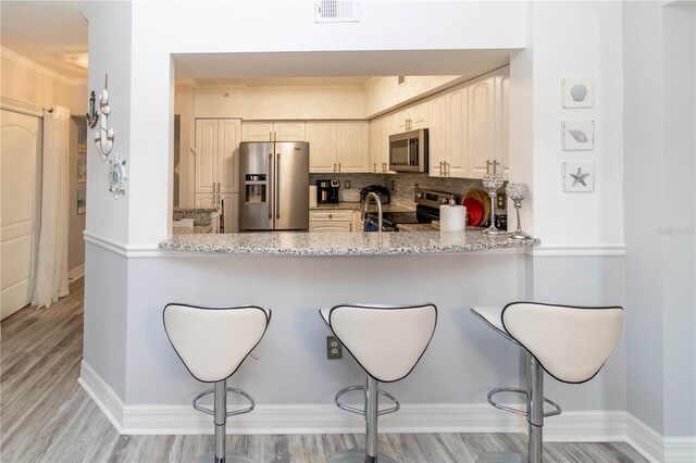 kitchen featuring light stone countertops, appliances with stainless steel finishes, a kitchen bar, and kitchen peninsula