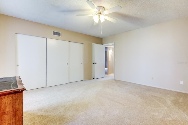 unfurnished bedroom with ceiling fan, a closet, light carpet, and a textured ceiling