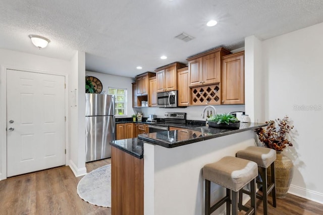 kitchen with stainless steel appliances, kitchen peninsula, dark stone counters, a breakfast bar area, and hardwood / wood-style flooring