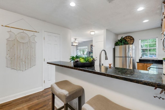 kitchen with dark hardwood / wood-style flooring, stainless steel refrigerator, ceiling fan, and dark stone counters