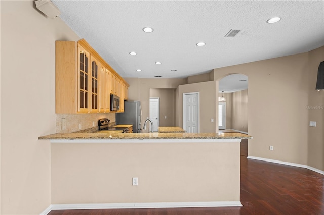 kitchen featuring kitchen peninsula, a textured ceiling, dark hardwood / wood-style floors, and stainless steel appliances