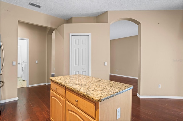 kitchen featuring a textured ceiling, washer / clothes dryer, a center island, and dark hardwood / wood-style floors