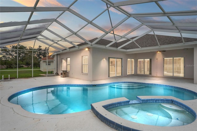 pool at dusk with an in ground hot tub, glass enclosure, and a patio area