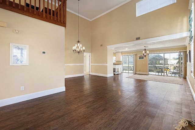 unfurnished living room featuring dark hardwood / wood-style flooring, a notable chandelier, crown molding, and a towering ceiling