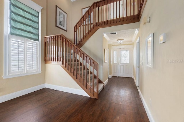 entryway with a high ceiling, ornamental molding, and dark wood-type flooring