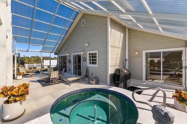 rear view of house featuring a patio, glass enclosure, and an in ground hot tub