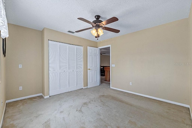 unfurnished bedroom with light carpet, ceiling fan, a closet, and a textured ceiling