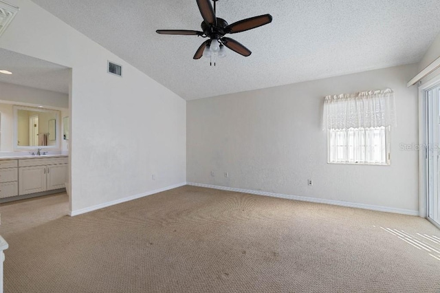 unfurnished bedroom featuring lofted ceiling, sink, light colored carpet, and a textured ceiling